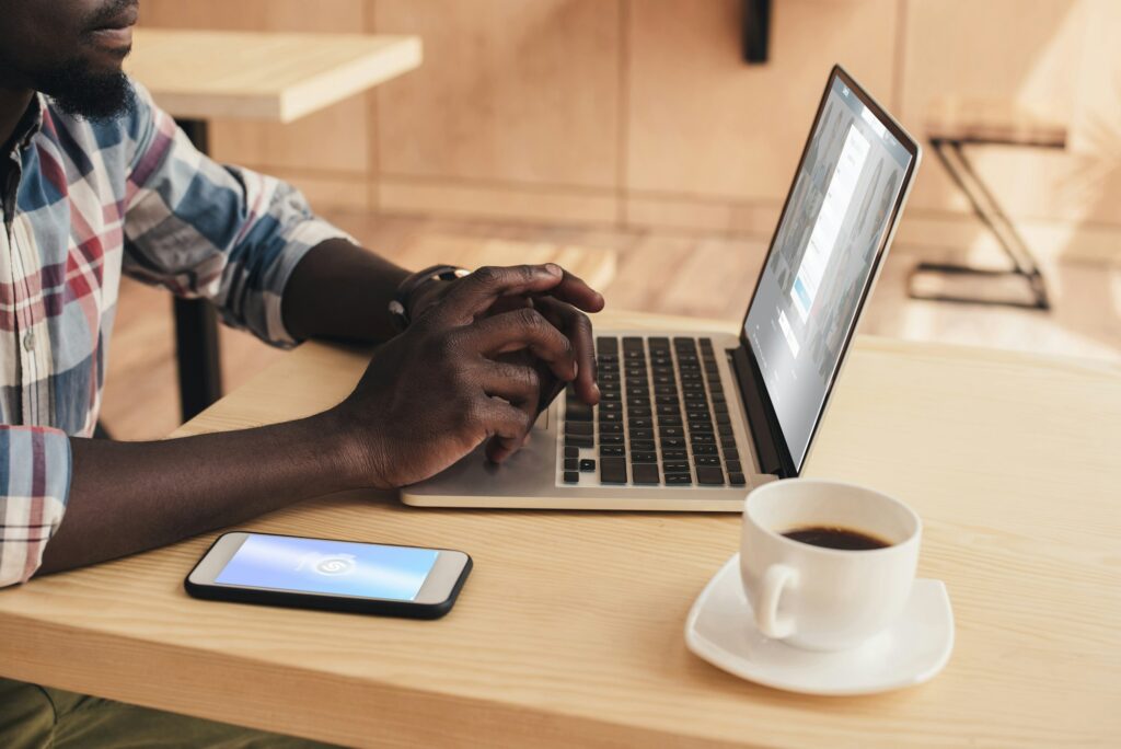 cropped view of african american man using smartphone with shazam and laptop with linkedin website