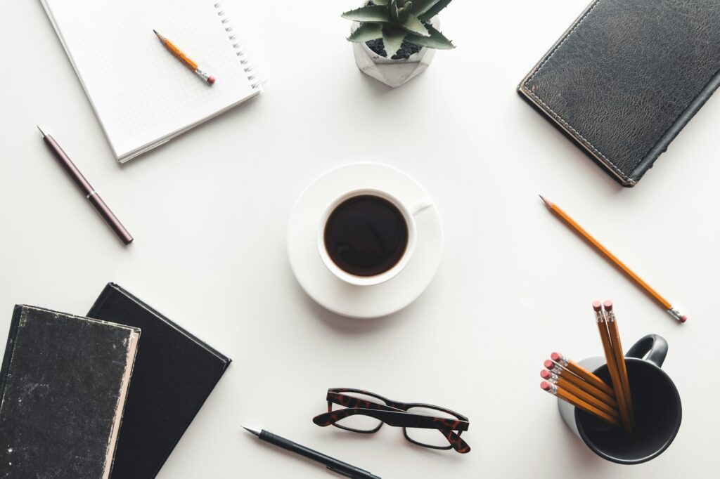 Office desk table with supplies, coffee cup and flower. Top view