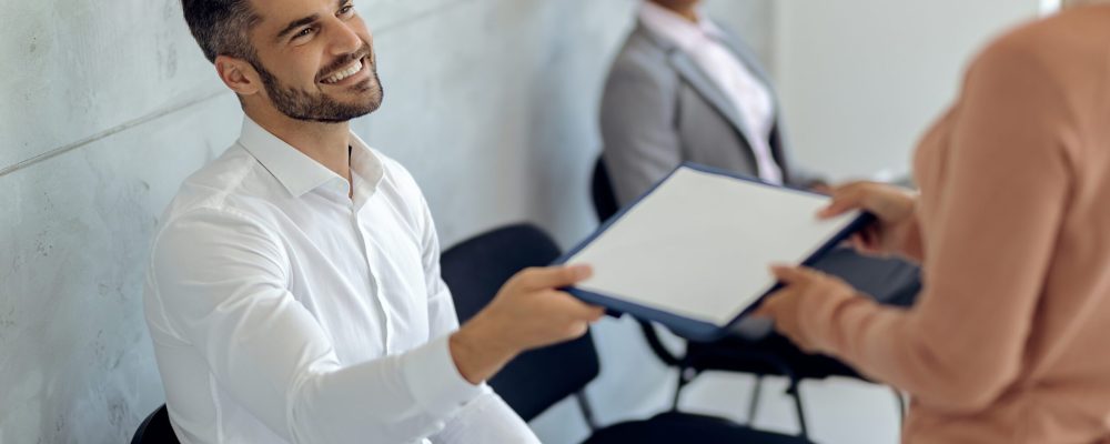 Happy businessman giving his resume while waiting for job interview in a hallway.